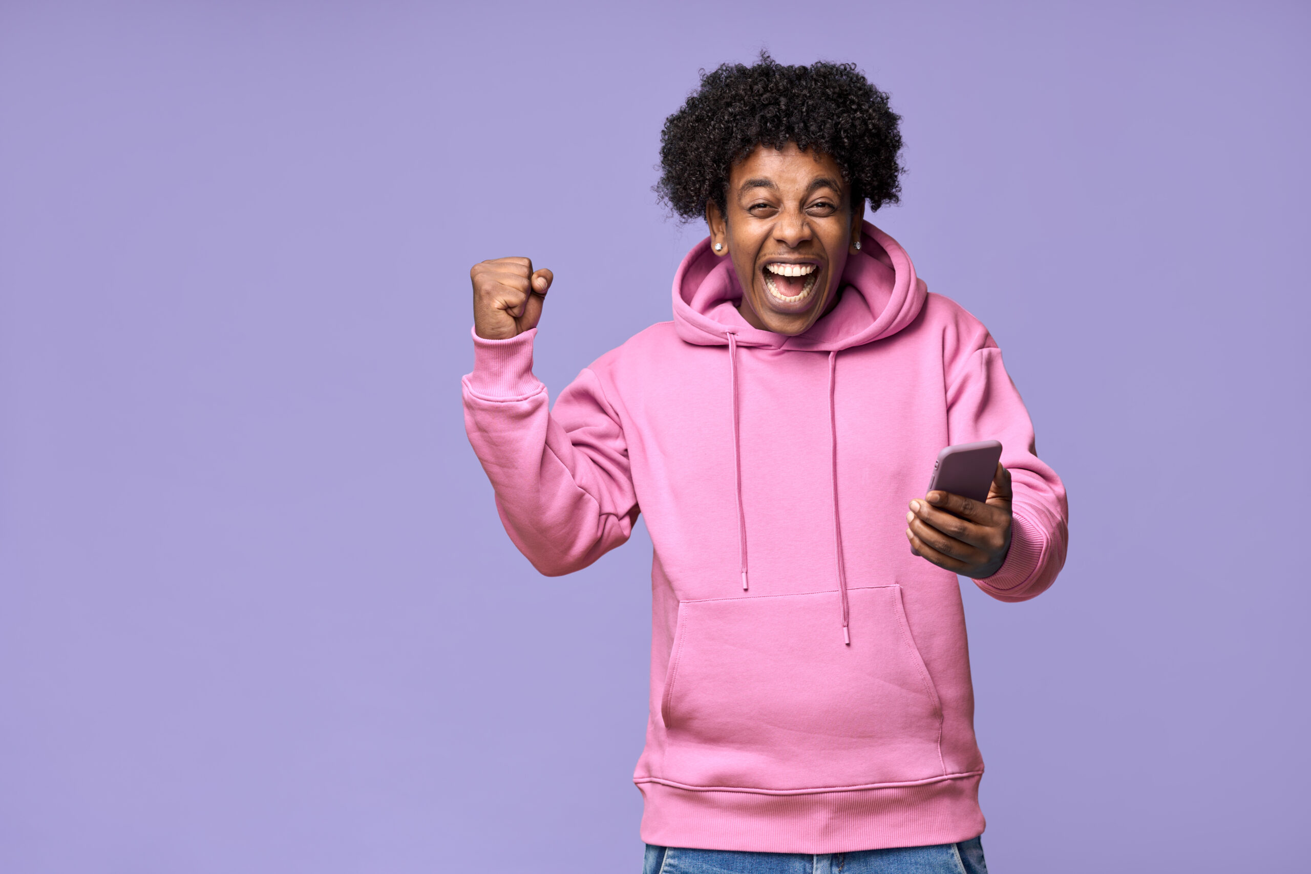 Excited happy African teen guy winner holding cell phone winning game online.